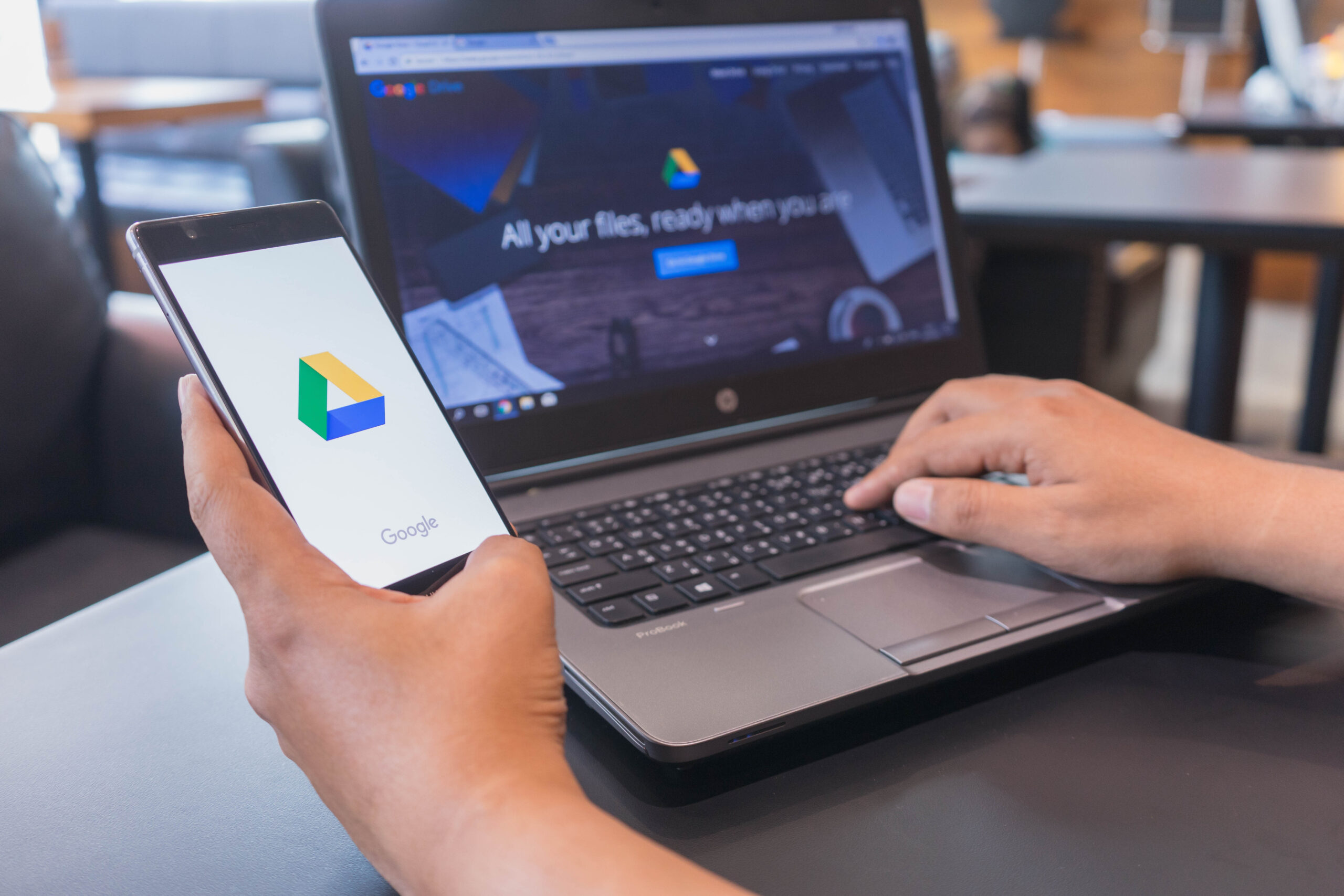 man holding smartphone on left hand and typing on laptop with right hand